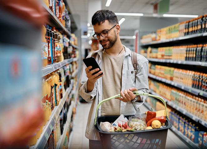 jeune homme qui regarde son téléphone en faisant ses courses